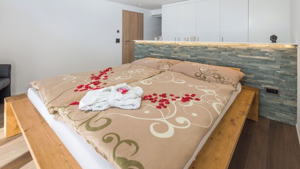 Ein modernes Schlafzimmer mit einem Steinkopfteil, einem Holzbettgestell und einem ordentlich bezogenen Bett mit Handtuch und Rosenblüten.