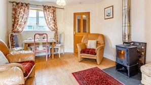 A cozy room with a fireplace, a dining table with chairs, a window with curtains, and a door. - 2 Bed in Inverness (oc-44481) (Drumnadrochit)