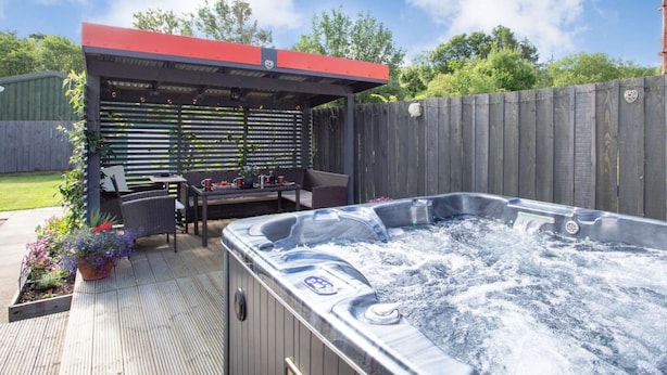 A hot tub with a wooden deck, a covered seating area, and a wooden fence in the background. - 2 Bed in Inverness (oc-44481) (Drumnadrochit)