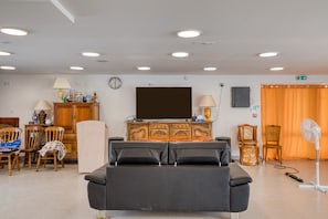 Une pièce avec un canapé noir, un meuble en bois et un téléviseur fixé au mur.