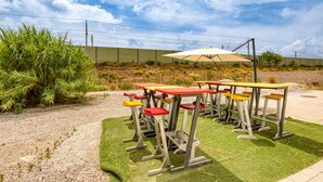 Terrasse mit Tischen und Stühlen, eine Rasenfläche und blauer Himmel.