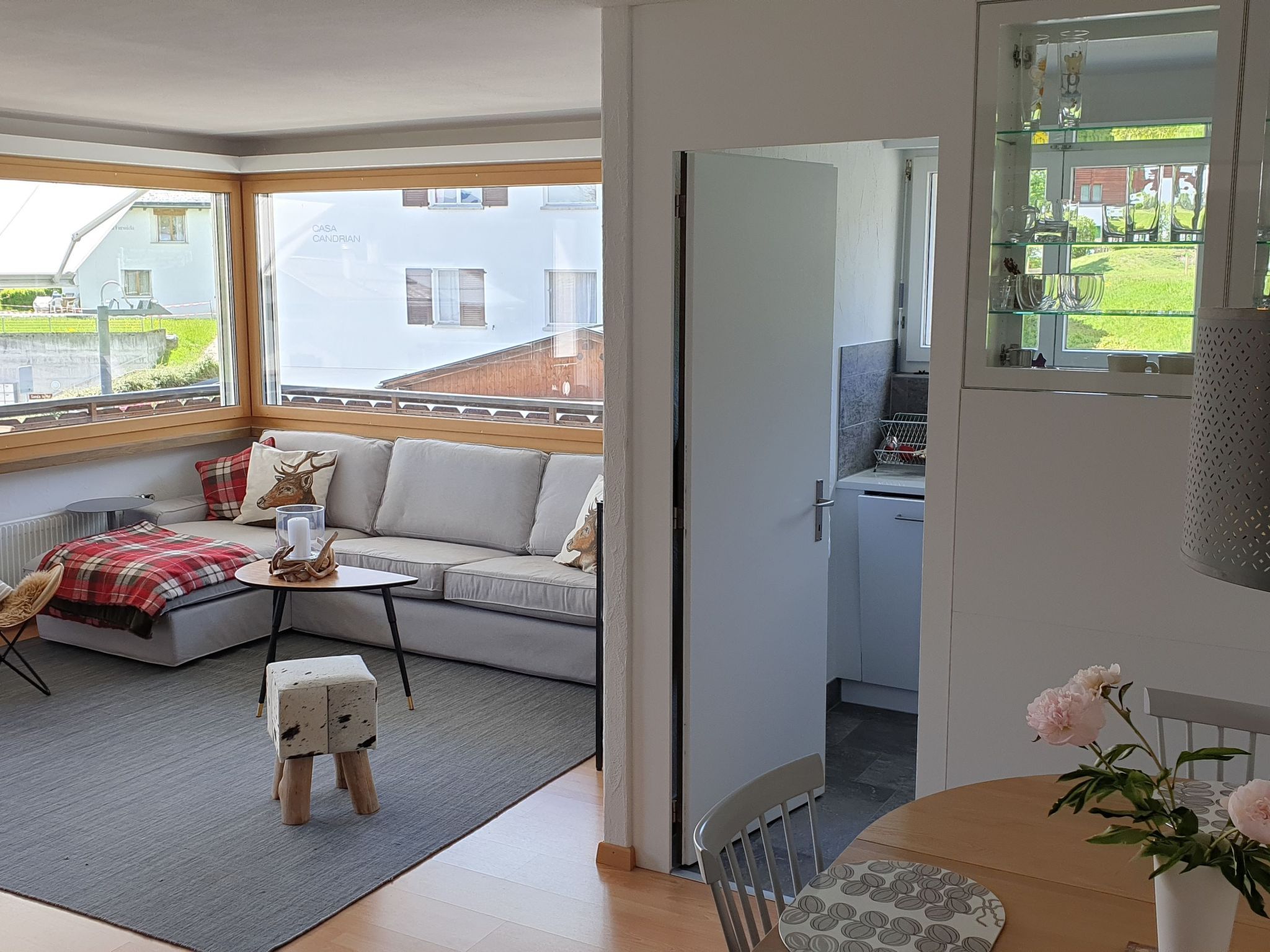 Ein modernes Wohnzimmer mit einer Couch, einem Couchtisch und einem kleinen Hocker. Ein Fenster bietet Blick auf eine Wohngegend.