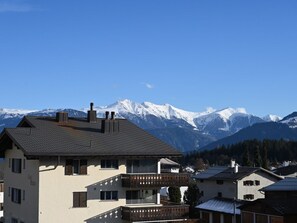 Ein Wohngebäude mit Balkon, Bergkulisse und blauem Himmel.