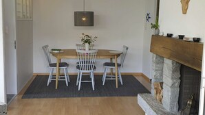 Ruokailutilassa on puinen pöytä, neljä tuolia, riippuvalaisin, takka ja kiviseinä.