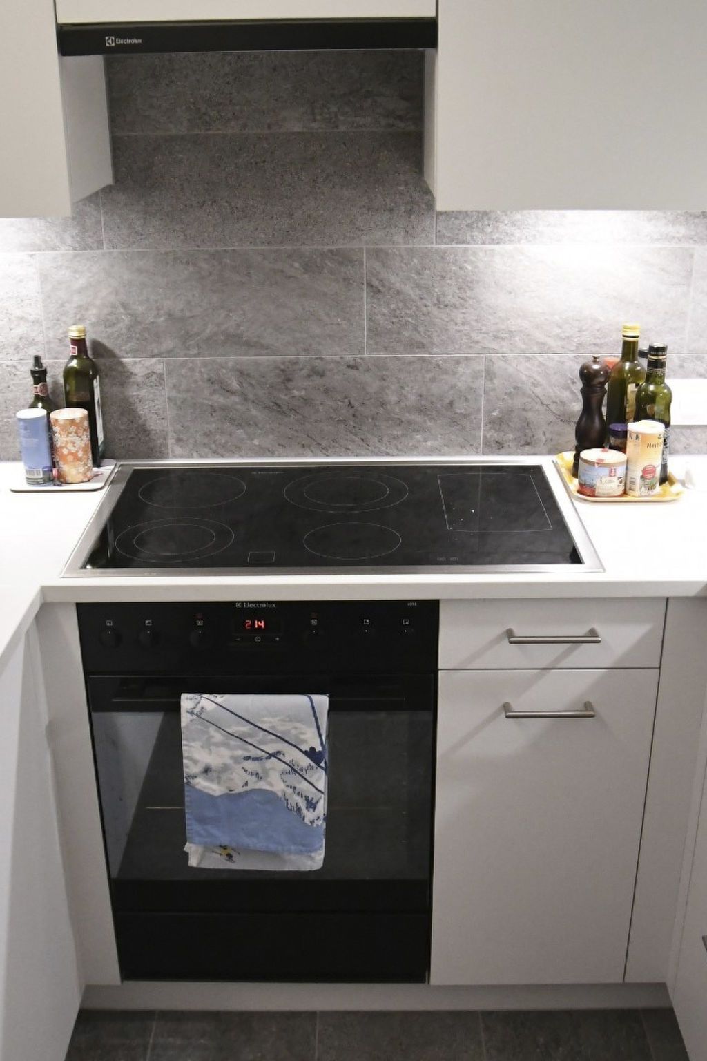 A kitchen with a black induction cooktop, a built-in oven, and a microwave. There are bottles and a container on the countertop.