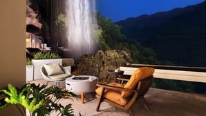 Un balcón con vista a una cascada, una silla blanca, una silla de madera y una mesita.