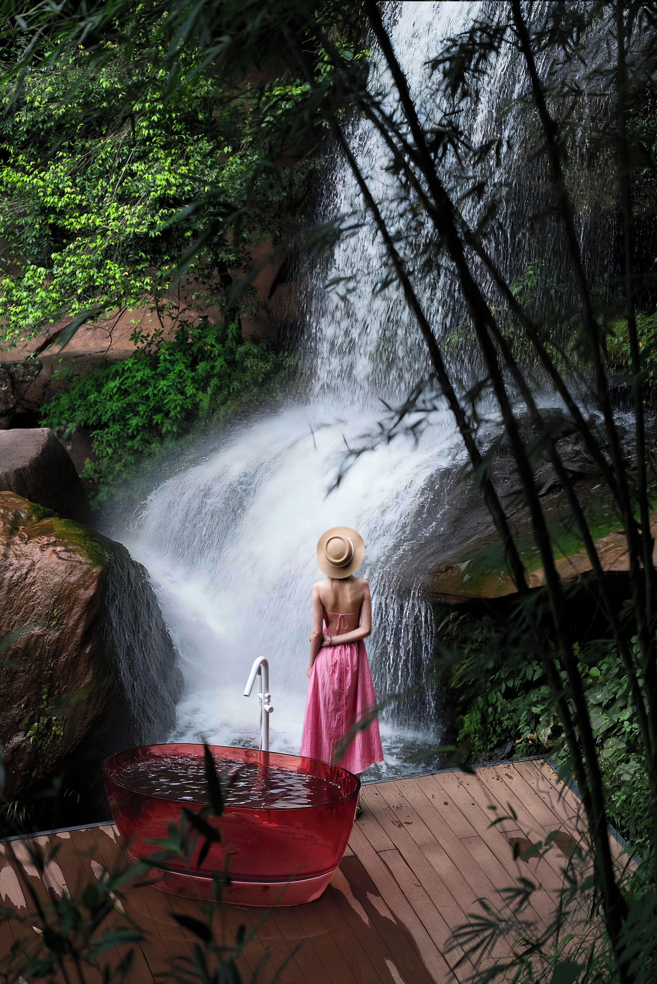 A woman in a pink dress and straw hat standing by a waterfall.