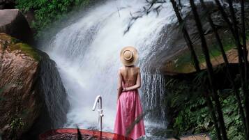A woman in a pink dress and straw hat standing by a waterfall.