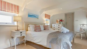 Ein Schlafzimmer mit Bett, Nachttischen, Kommode, Stuhl, Fenster und einem Bild an der Wand.