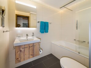 Un baño moderno con lavamanos blanco, tocador de madera, cabina de ducha de vidrio y un inodoro.