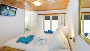 Een slaapkamer met een houten bed, een televisie aan de muur en een raam met zonwering.