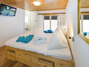 A bedroom with a wooden bed, a television on the wall, and a window with blinds. - Touring Cheminée, (Grächen), 1929 by Interhome (Grächen)