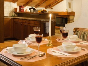 Ein Esszimmertisch ist gedeckt mit weißen Tellern, Schüsseln und Besteck, Gläsern mit roter Flüssigkeit, vermutlich Wein, und einer Kerze in einem Messinghalter.
