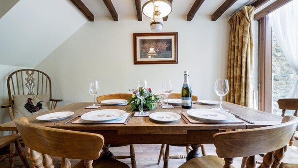 Una tavola da pranzo imbandita per quattro, con sedie, un lampadario, un quadro appeso al muro e una bottiglia di champagne.