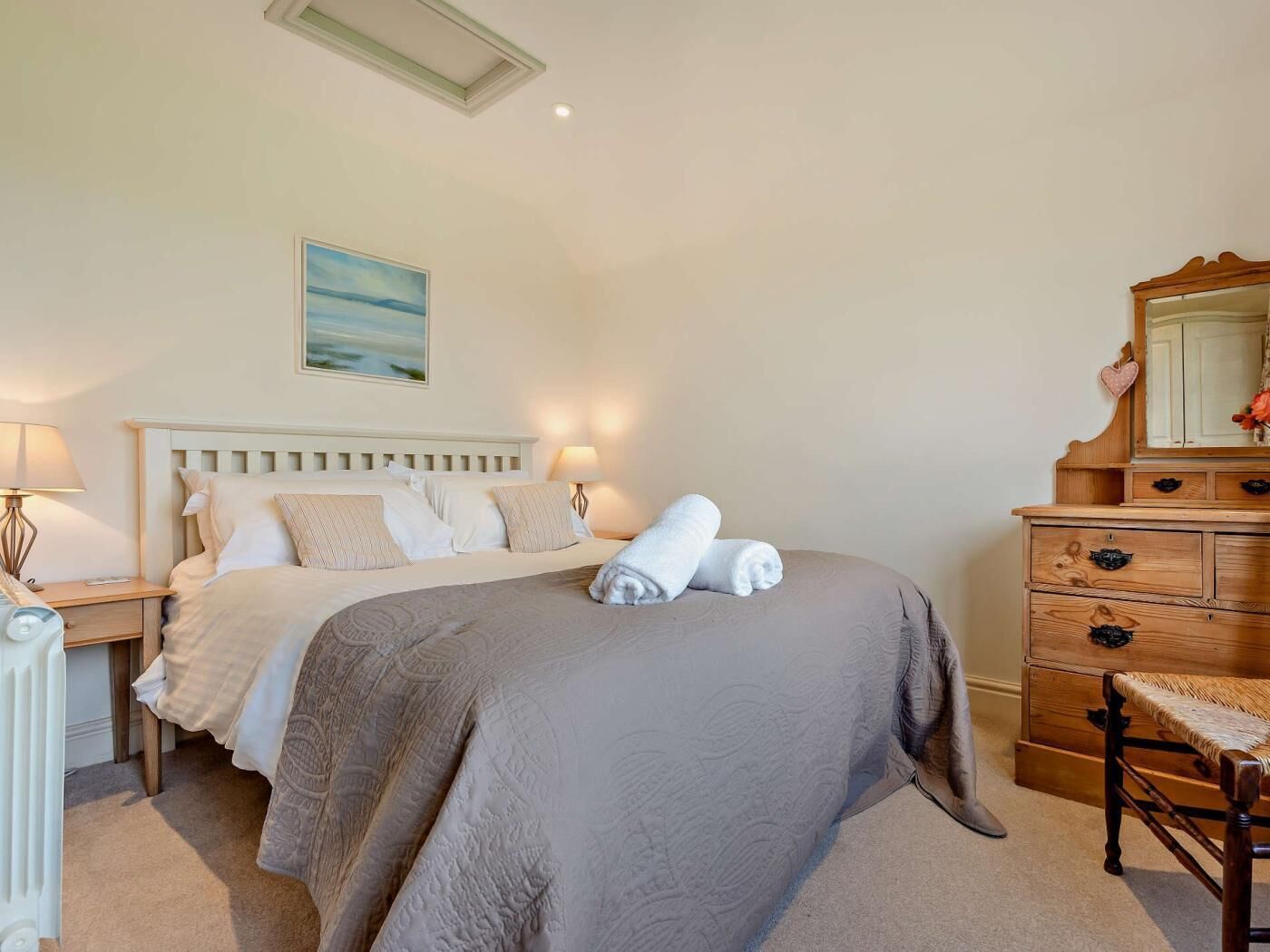 A bedroom with a bed, bedside lamps, a dresser, a mirror, and a painting on the wall.