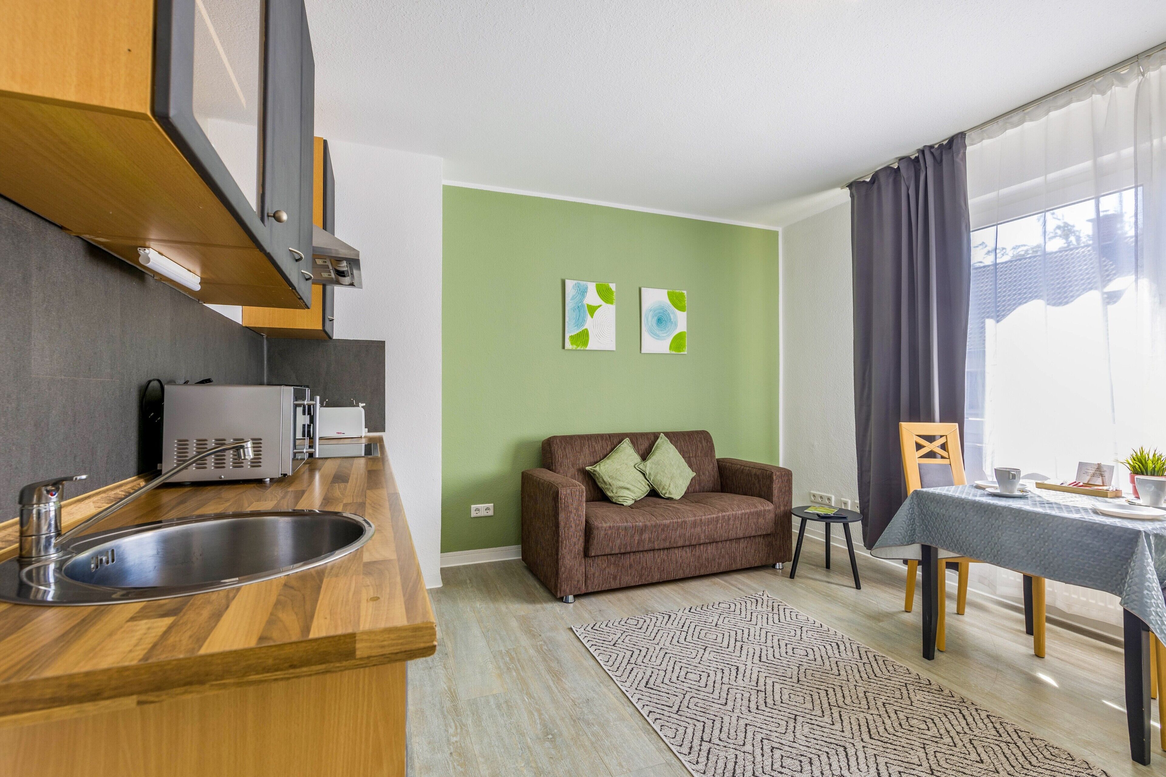 A compact living space with a kitchenette, a sofa, a dining table, and a patterned rug.