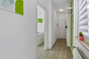 A hallway with a bed, a door, a radiator, and a plant on a shelf.