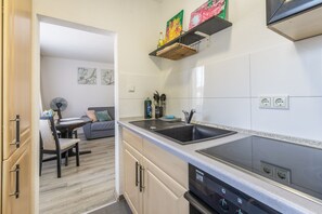 A modern kitchen with a black stove, a sink, and a dishwasher. There is a dining area with a table and chairs. - Apartment 'RheinStay Business' with Private Terrace, Balcony and Wi-Fi (Duisburg)