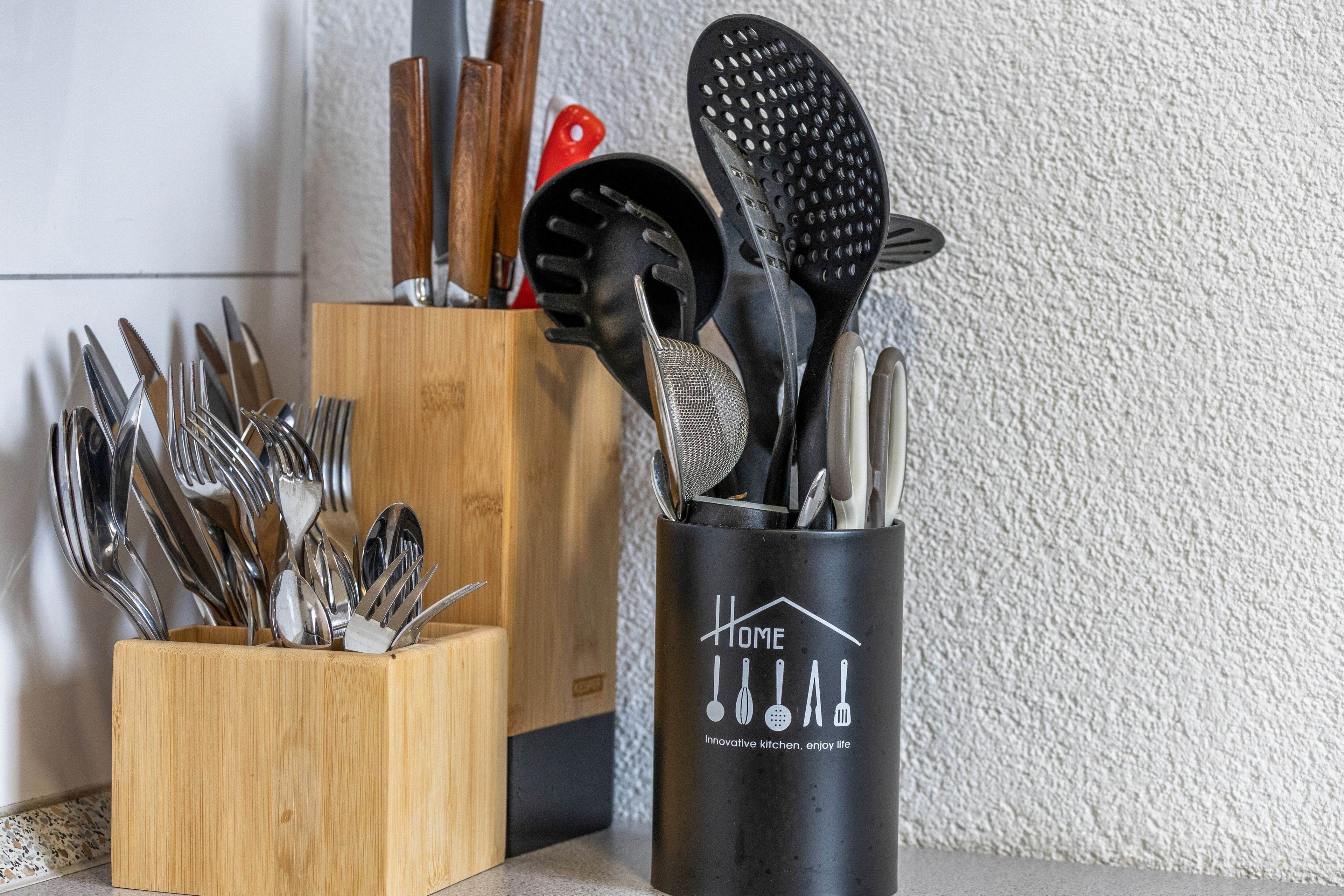 A kitchen utensil holder with various utensils, including a spatula and a grater, and a wooden utensil block.