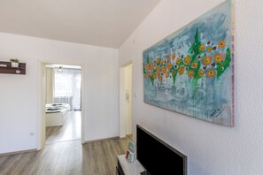 Uma sala de estar moderna com uma TV de tela plana, um quadro de flores e um corredor que dá para uma sala de jantar.