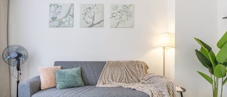 A living room with a grey sofa, a fan, a lamp, and a potted plant.