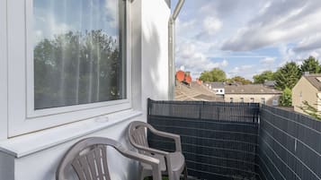 Un balcón con vista a una zona residencial, una valla negra y una silla de plástico.