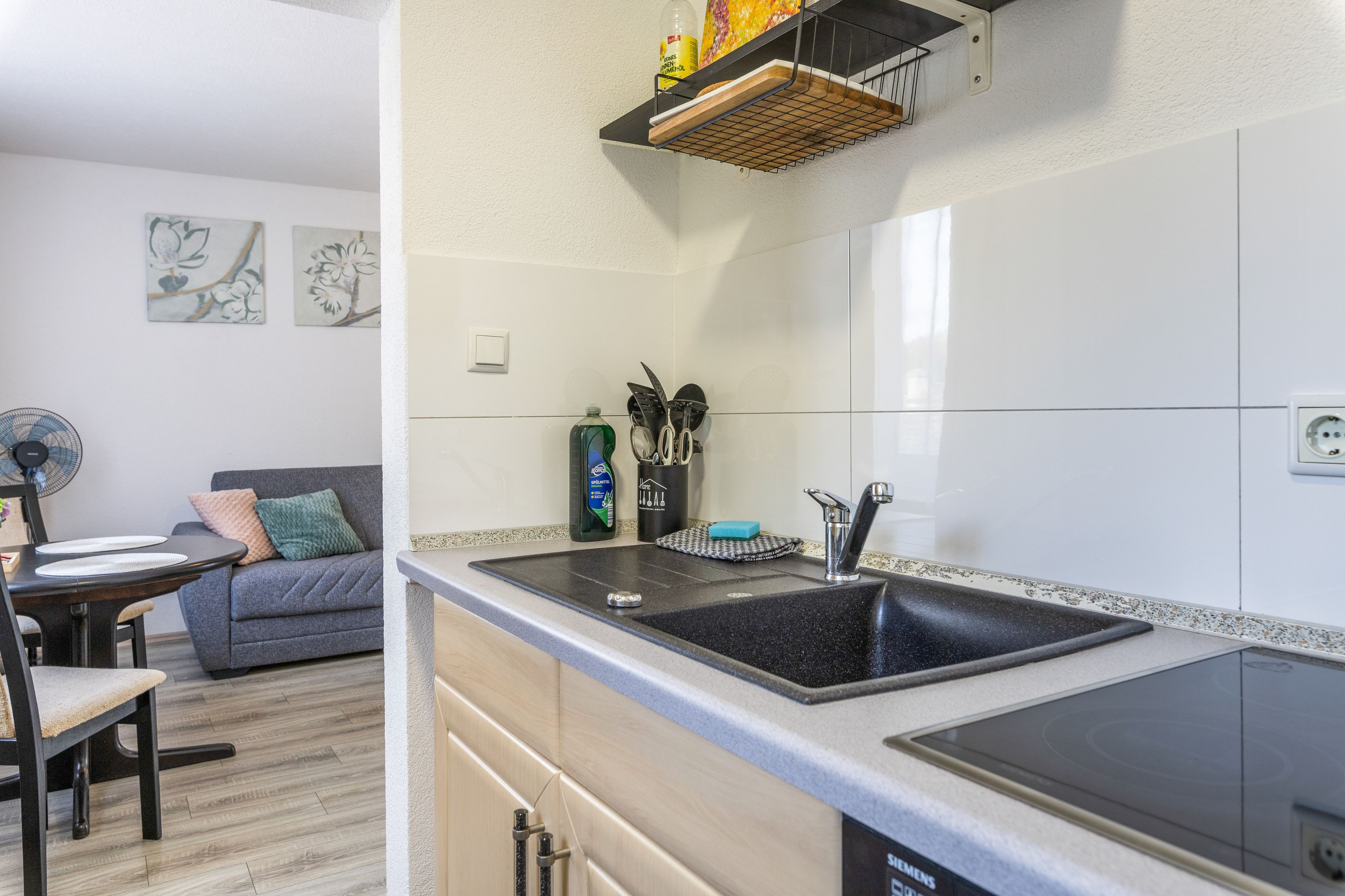 Eine moderne Küche mit einer schwarzen Spüle, einem eingebauten Backofen und einem Essbereich mit einem grauen Sofa und einem Tisch.