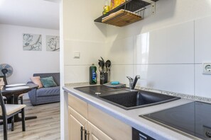 Una cocina moderna con un lavamanos negro, horno empotrado y comedor con sofá gris y una mesa.
