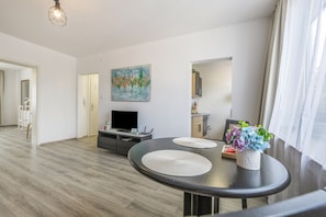 A modern living room with a flat-screen TV, a painting, and a dining area with a table and chairs. - Apartment 'RheinStay Business' with Private Terrace, Balcony and Wi-Fi (Duisburg)