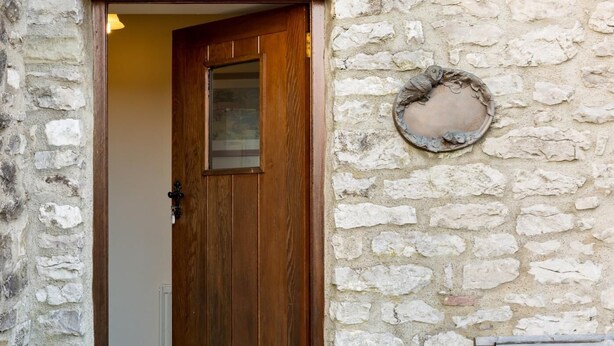 Un mur de pierre avec une porte en bois, une plaque de pierre ronde et un banc.