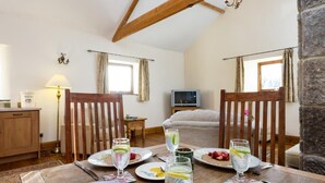 Un coin repas avec une table dressée pour quatre personnes, un téléviseur en arrière-plan et un lit avec vue.