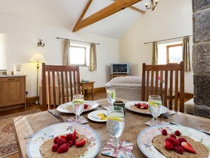 Ein Essbereich mit Tisch für vier Personen, einem Fernseher im Hintergrund und einem Bett mit Blick.
