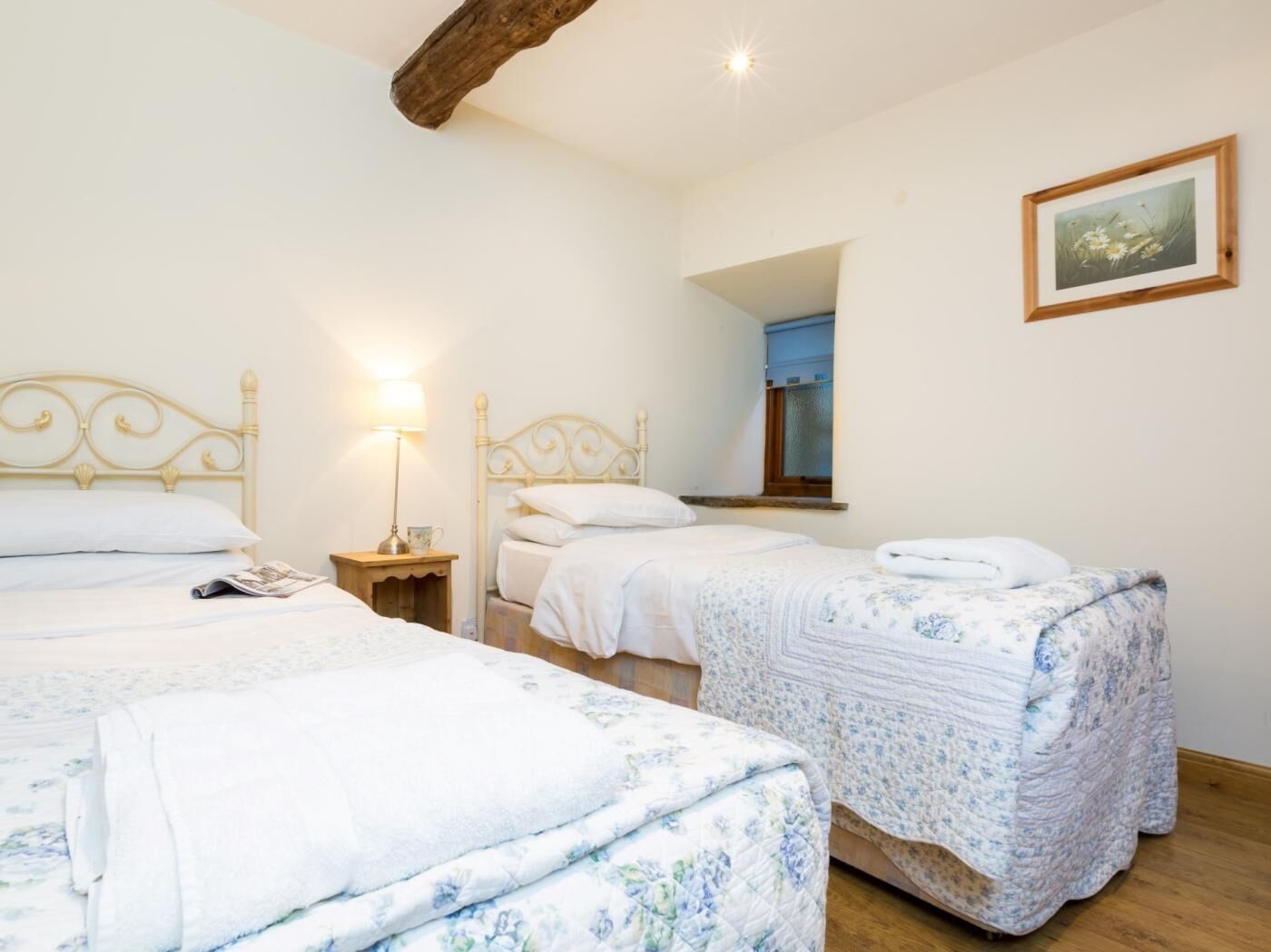 Slaapkamer met twee bedden, een nachtkastje met lamp, een ingelijst schilderij aan de muur en een raam met uitzicht.