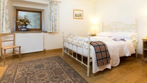 Une chambre à coucher avec un lit, une fenêtre avec des rideaux, un radiateur, une chaise en bois et un tapis.
