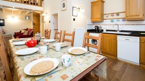A dining area with a table set for four, wooden chairs, a red teapot, and a kettle. There is a kitchen area with wooden cabinets and a dishwasher. - 4 Bed in High Peak (oc-pk630) (Chapel-en-le-Frith)