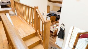 A wooden staircase leading to a dining area with a table set for two, a kitchen visible in the background, and a coat rack by the door. - 4 Bed in High Peak (oc-pk630) (Chapel-en-le-Frith)