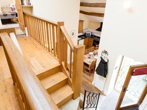 Eine Holztreppe führt zu einem Essbereich mit einem für zwei Personen gedeckten Tisch, im Hintergrund ist eine Küche zu sehen, und in der Nähe der Tür steht ein Kleiderständer.