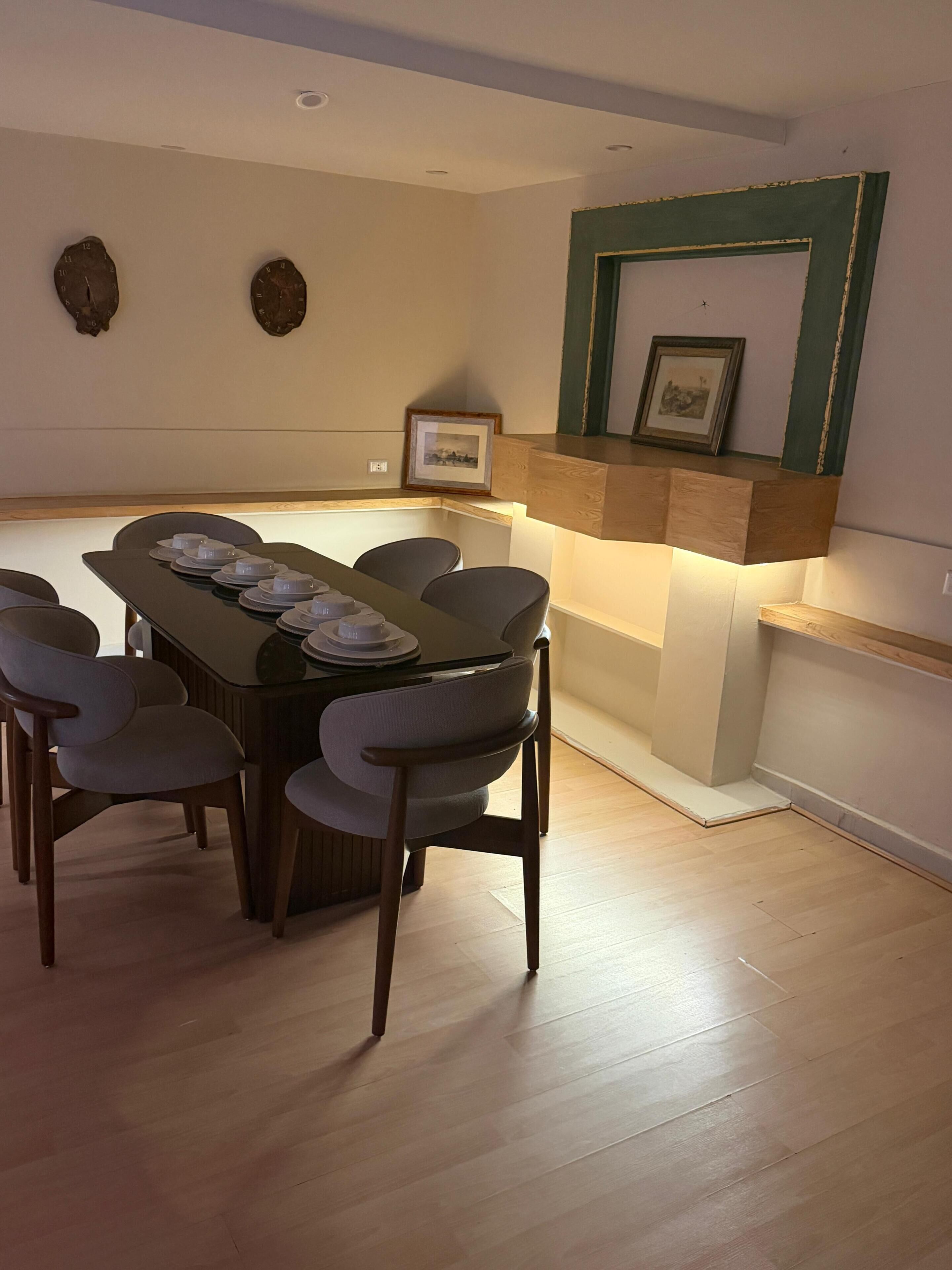 A dining area with a wooden table, six chairs, and a built-in shelf with framed pictures.