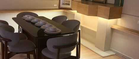 A dining area with a wooden table, six chairs, and a built-in shelf with framed pictures.