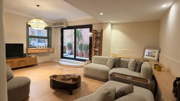 Ein Wohnzimmer mit Sofa, Couchtisch, Fernseher, Bücherregal und einem Fenster mit Blick auf einen Innenhof.