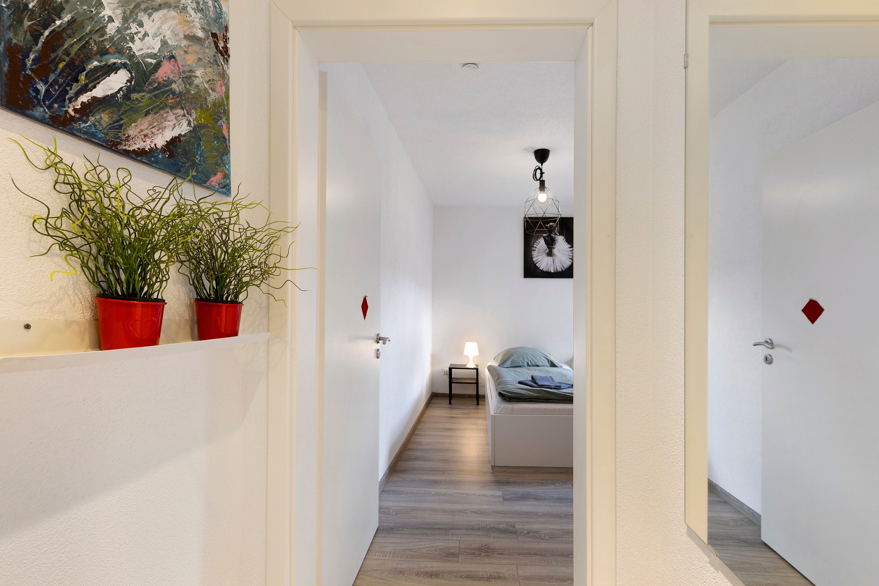 Ein Flur, der zu einem Schlafzimmer mit Bett, Nachttisch, Lampe und einem Bild an der Wand führt.