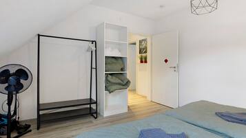 A bedroom with a bed, a standing fan, a vacuum cleaner, and a wardrobe.