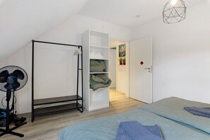 Ein Schlafzimmer mit einem Bett, einem Standventilator, einem Staubsauger und einem Kleiderschrank.
