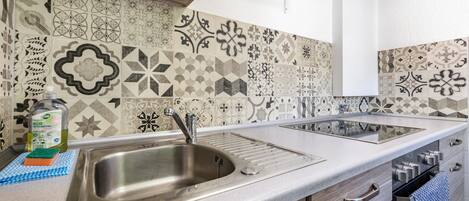 A kitchen with a stainless steel sink, a dish soap bottle, and a sponge on the counter.