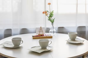 A round table with four white cups and saucers, a small vase with flowers, and a box of chocolates.