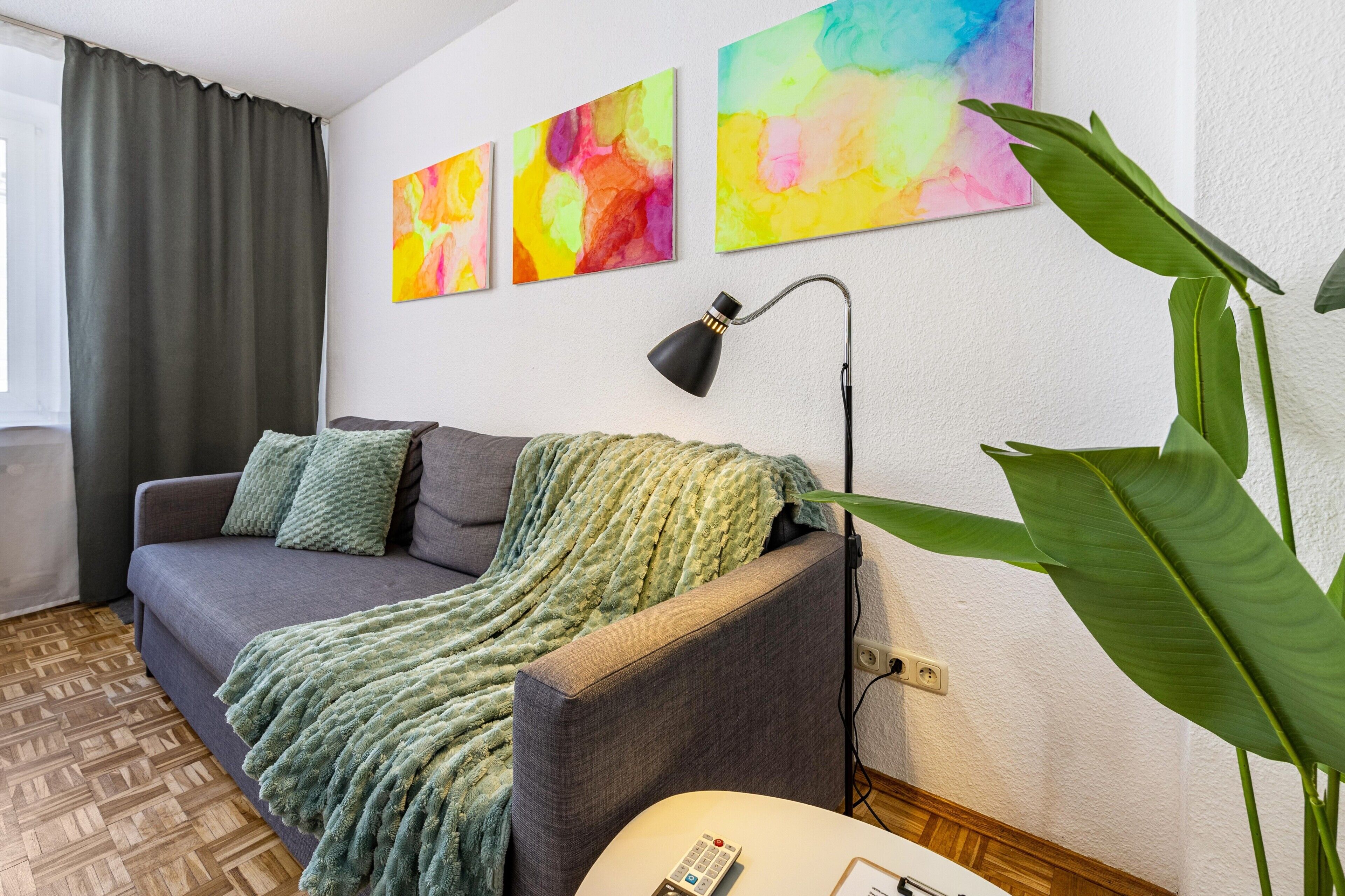 Un soggiorno moderno con un divano grigio, una coperta verde e una grande pianta verde.