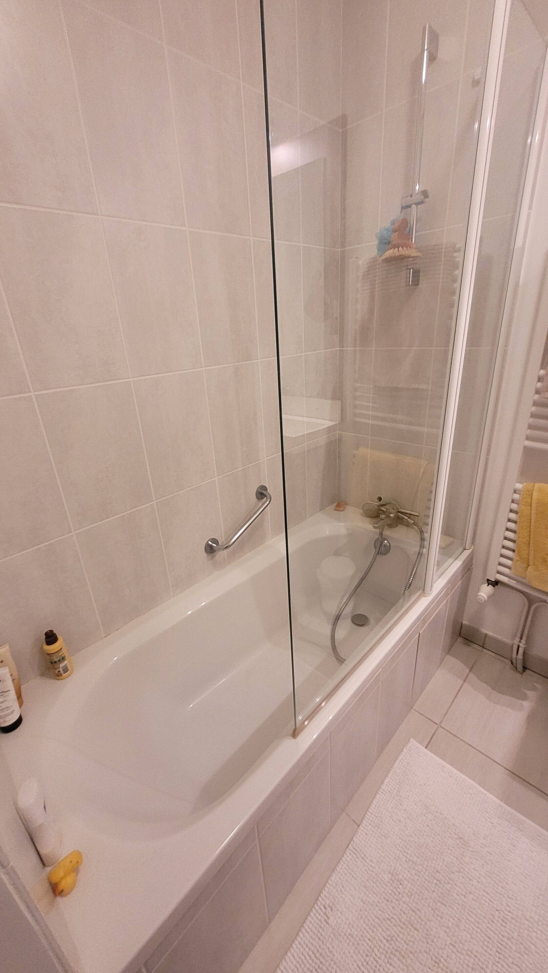 A modern bathroom with a glass-enclosed shower, a white bathtub, and a white tiled floor.