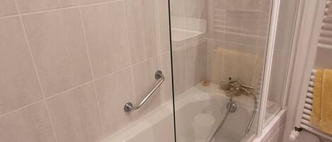 A modern bathroom with a glass-enclosed shower, a white bathtub, and a white tiled floor.