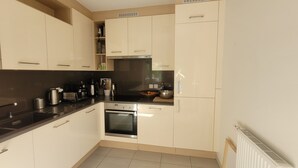Uma cozinha compacta com armários brancos, bancada preta, forno embutido e micro-ondas.