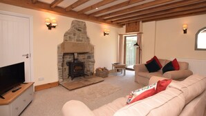 Ein gemütliches Wohnzimmer mit Kamin aus Stein, Holzbalken, Fernseher und einer Couch.